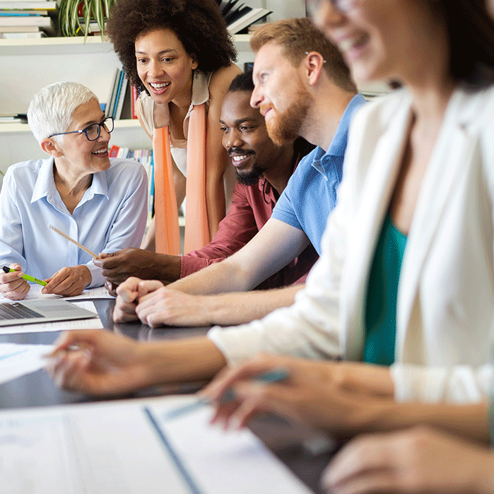 Diverse group of professionals collaborating around a table, smiling and engaged in discussion, symbolizing leadership development and teamwork