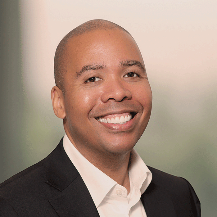 Portrait of Dr. David Brown Jr., smiling in a professional setting, wearing a black blazer and white shirt with a blurred background.