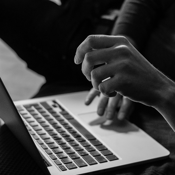 Black and white close-up of a person's hands typing on a laptop, symbolizing writing, creativity, and digital content creation.