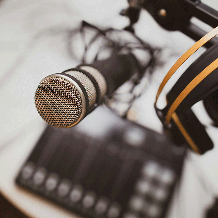 Close-up of a professional microphone and headphones with a blurred audio mixer in the background, symbolizing podcast recording and audio production.