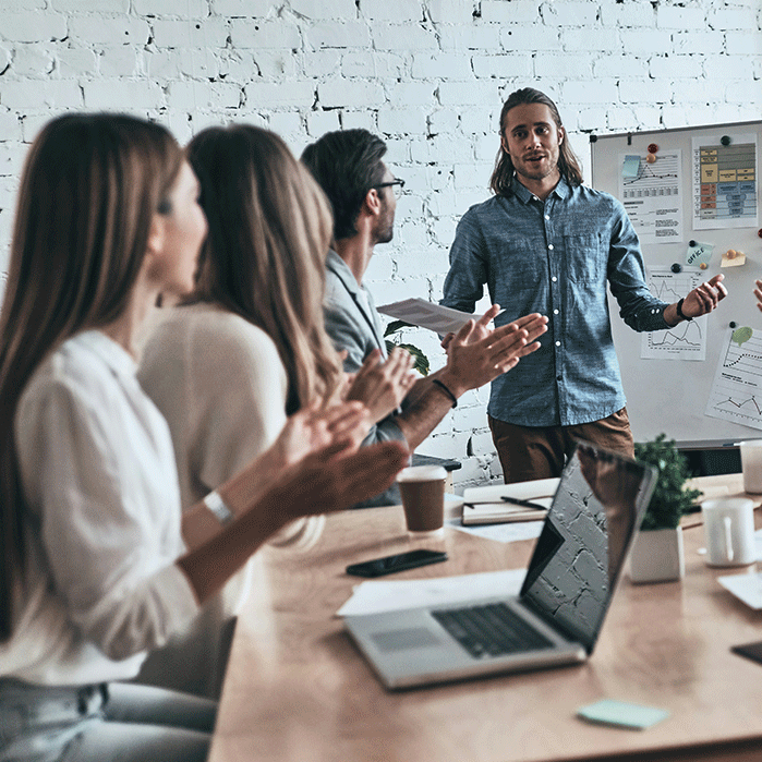 Team applauding a presenter during a meeting in a modern office, with a whiteboard displaying charts and graphs, symbolizing growth and leadership training.